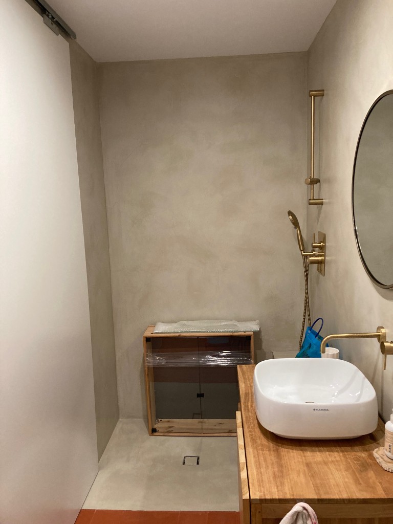 Aseo compacto con revestimiento microcemento beige sanitarios suspendidos y suelo terracota, La Floresta