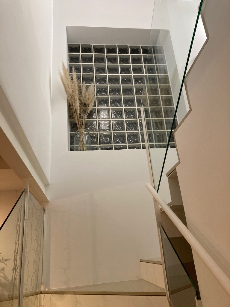 Escalera interior moderna con huellas claras barandilla de cristal y suelo de terracota, La Floresta