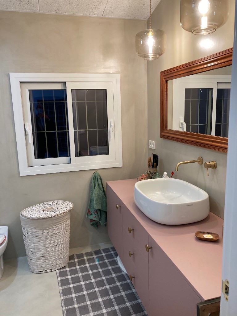 Baño con microcemento en paredes mueble lavabo rosa palo lavabo sobre encimera y grifería dorada, La Floresta