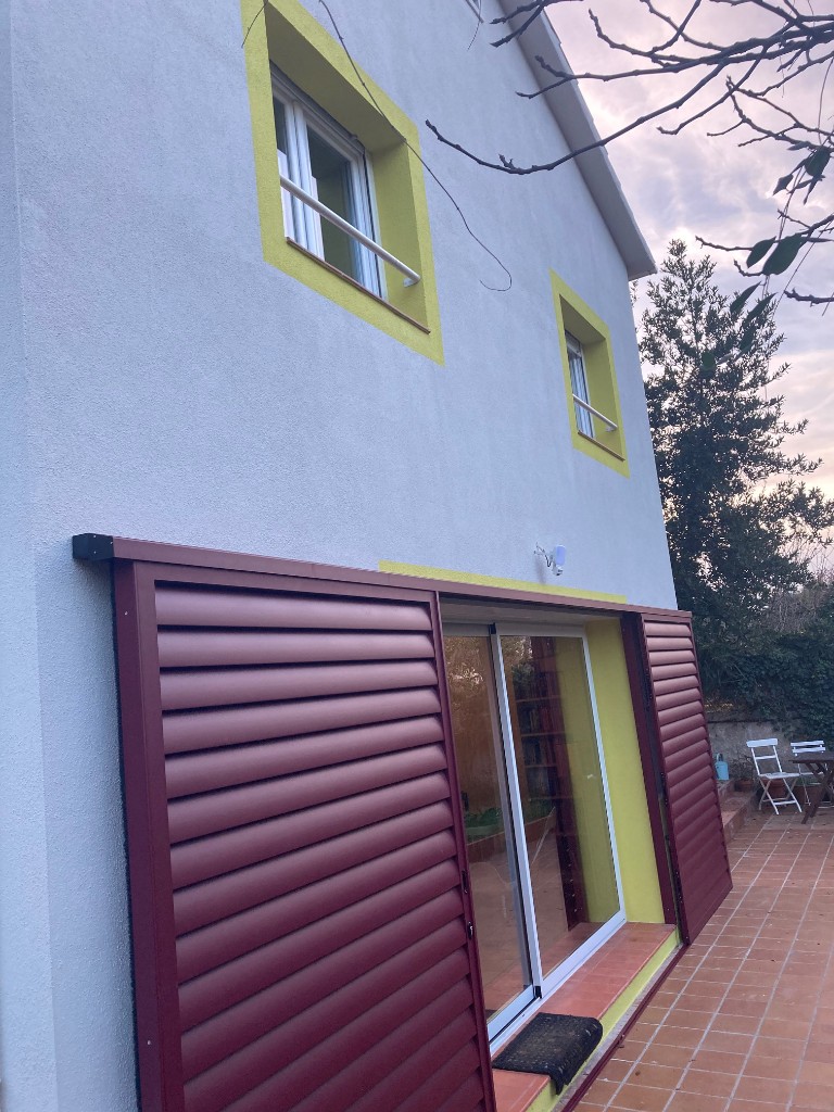 Fachada trasera con ventanas marco amarillo y contraventanas correderas, reforma La Floresta